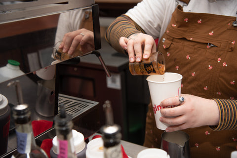 An image of someone pouring flavored syrup into a coffee cup